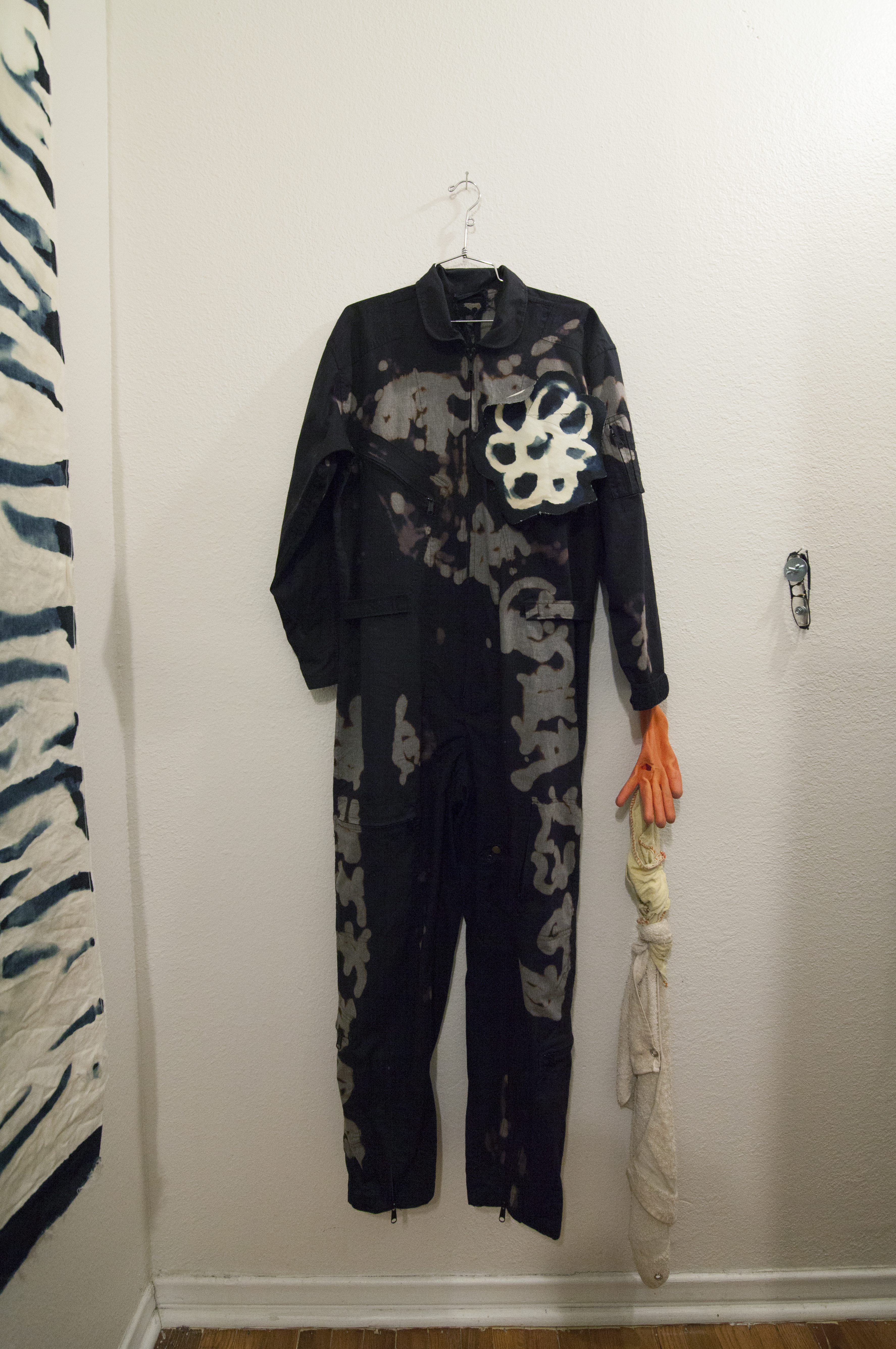 A dark jumpsuit with bleached patterns hung on a white wall